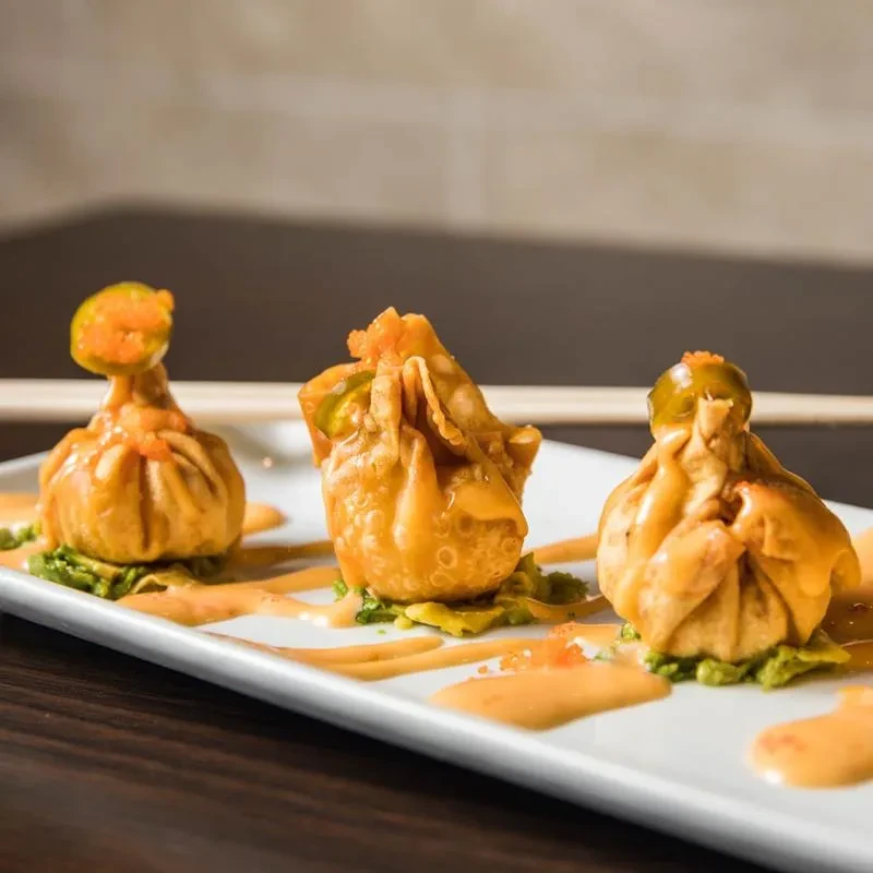 Three fried dumplings with green purée, orange sauce, roe, and pepper.