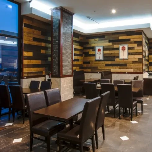 Empty restaurant interior with wood-plank walls, dark tables, and tiled floor.