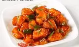 Plate of chili paneer with red sauce and green garnish.