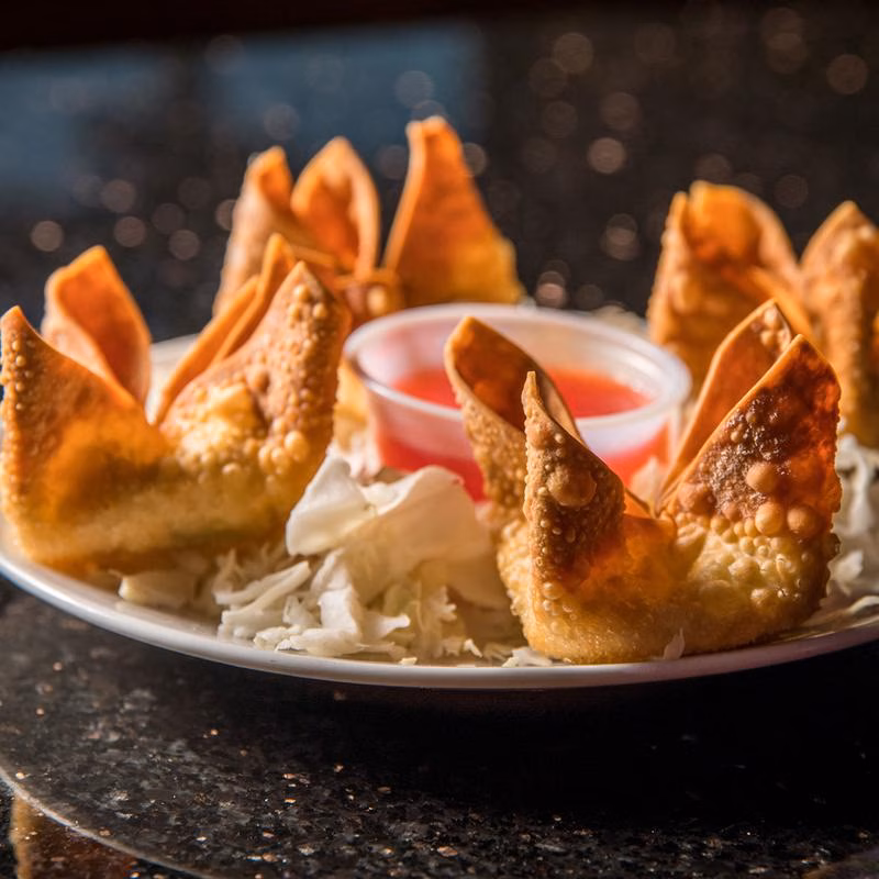 Fried wontons with shredded cabbage and red dipping sauce on a plate.