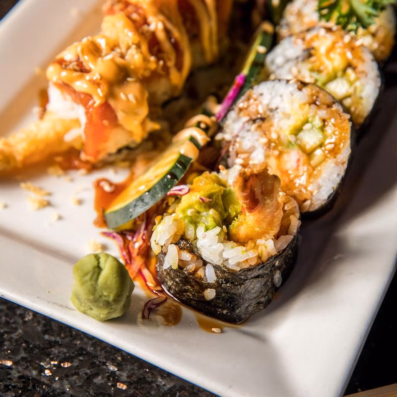 Plate of sushi rolls with tempura shrimp, avocado, and wasabi.