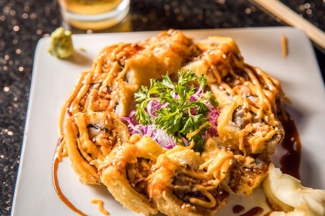 Deep-fried sushi rolls with sauce, sesame seeds, and garnish on plate.