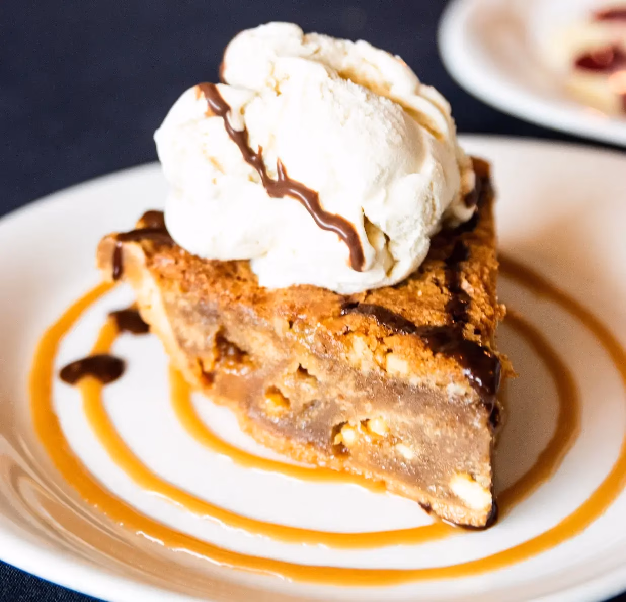 A slice of pie with vanilla ice cream, chocolate, and caramel sauce.