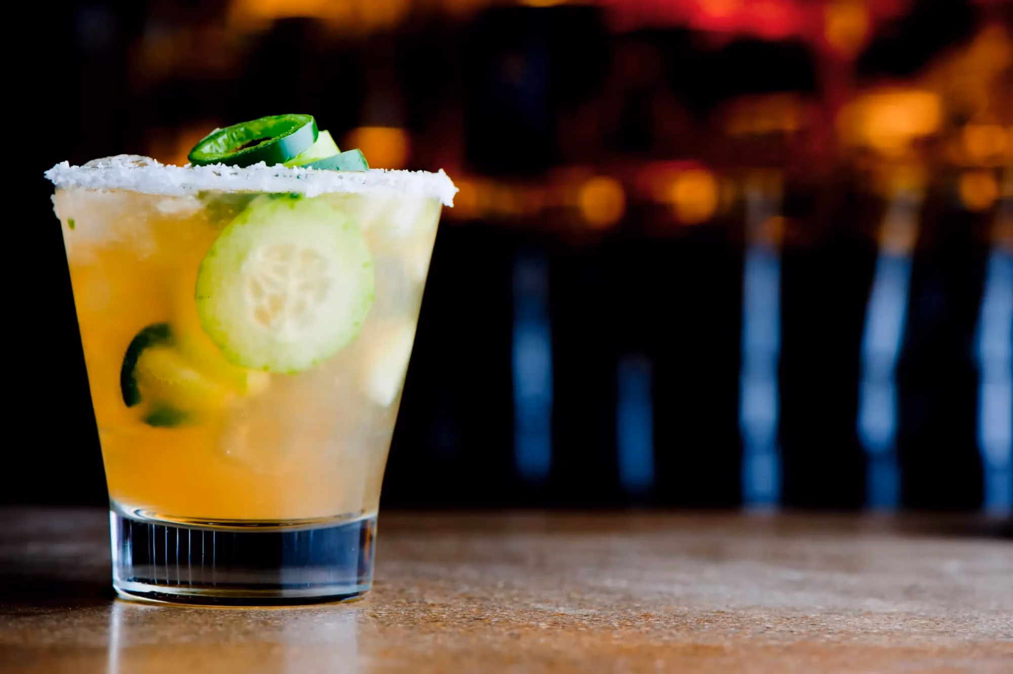 Glass of light drink with cucumber and jalapeño slices, salted rim.