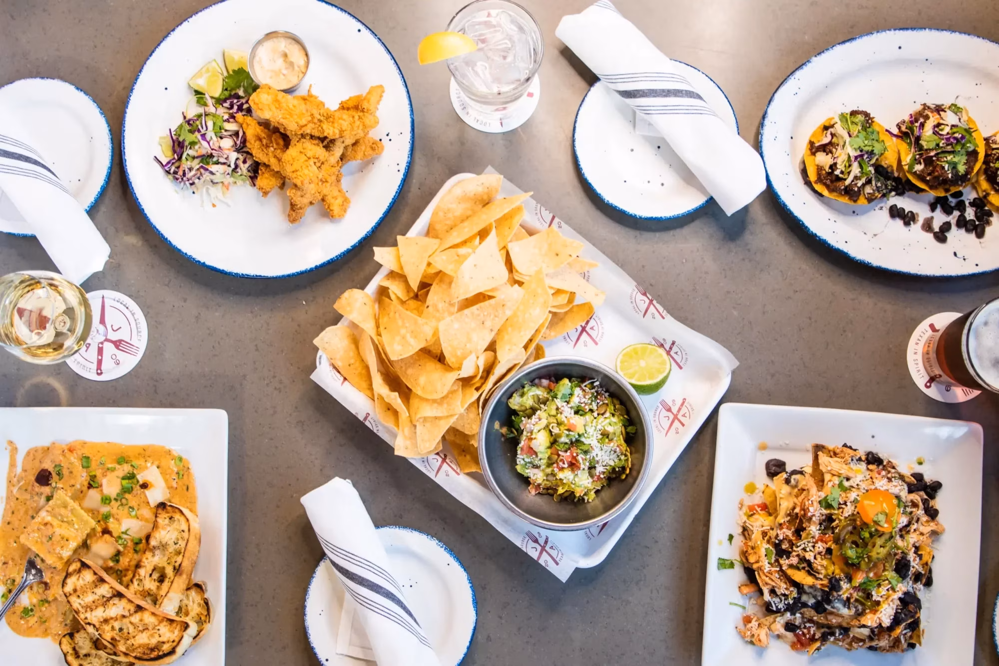 Overhead view of a table with fried chicken, nachos, tacos, and drinks.