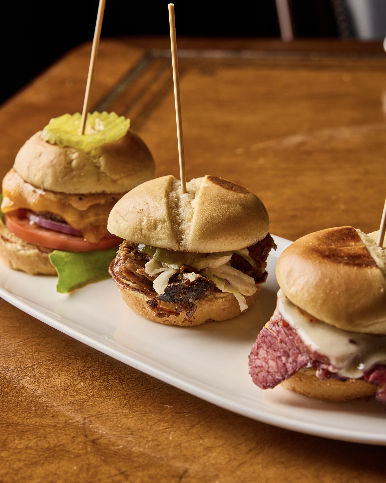 Three sliders: cheeseburger, pulled pork, and deli meat sandwich.
