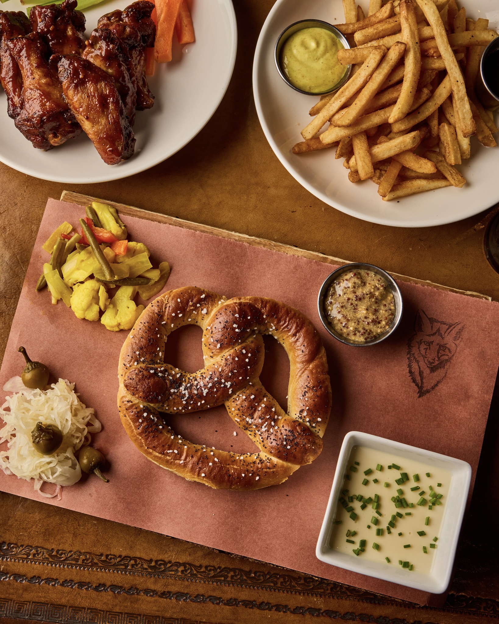 Plates of chicken wings, fries, pretzel, pickled vegetables, and sauces.