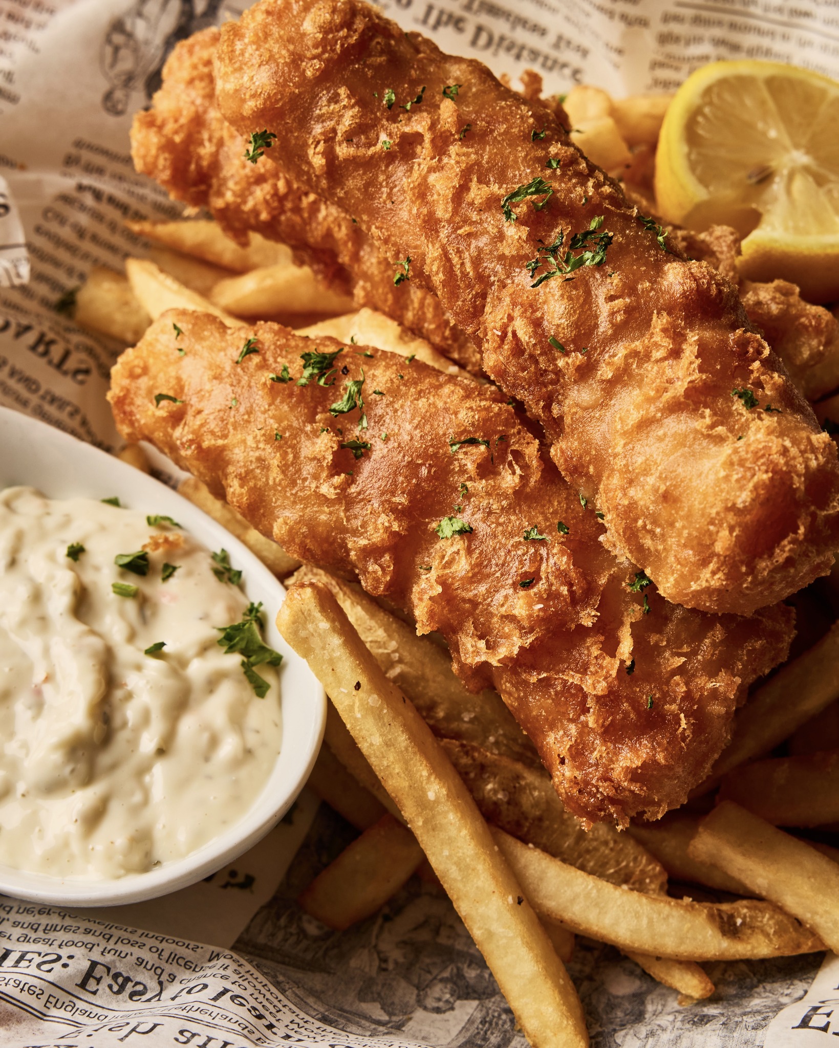 Golden-brown fish and chips with tartar sauce, lemon, and parsley.