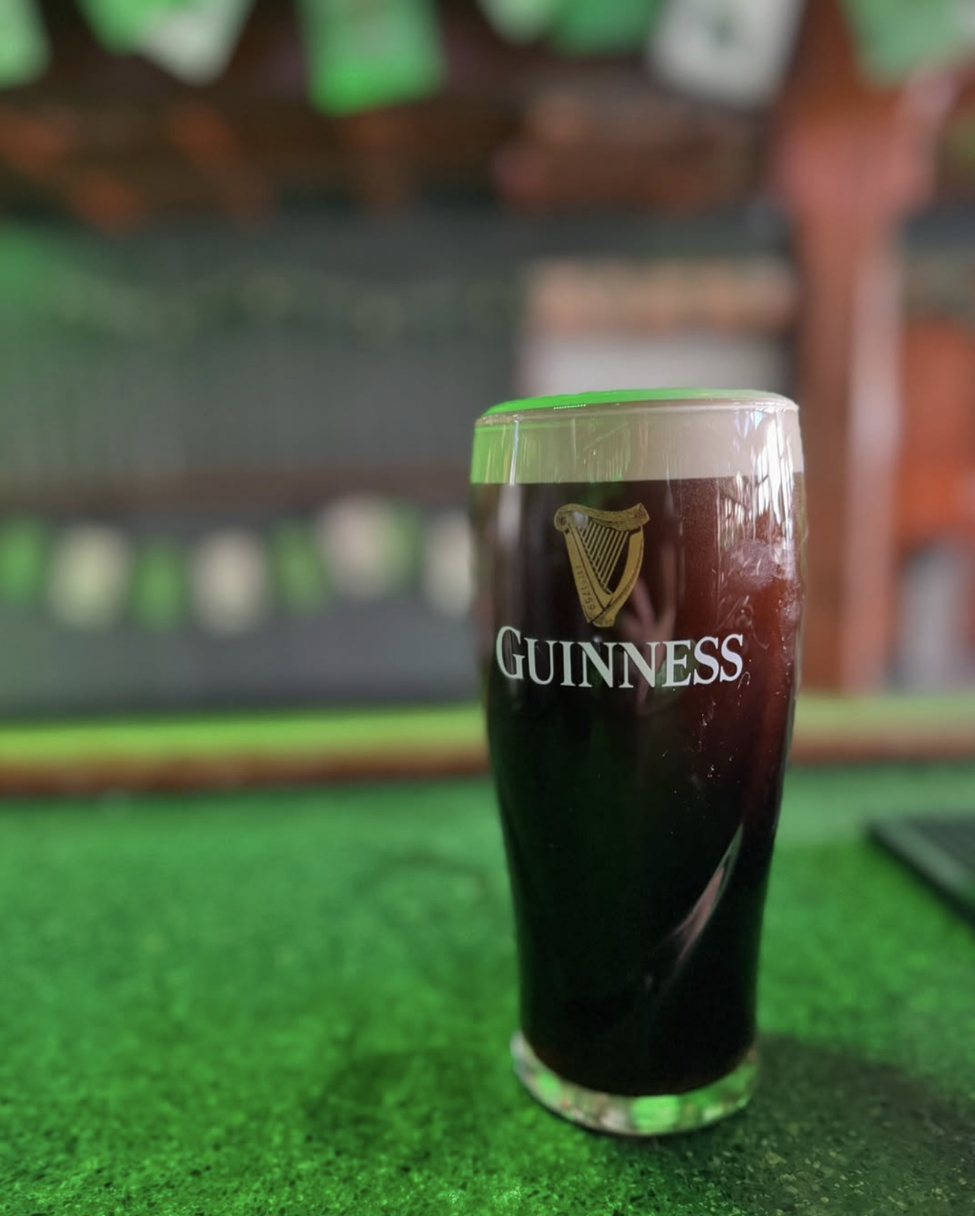 A glass of Guinness stout on a green bar top with foam.