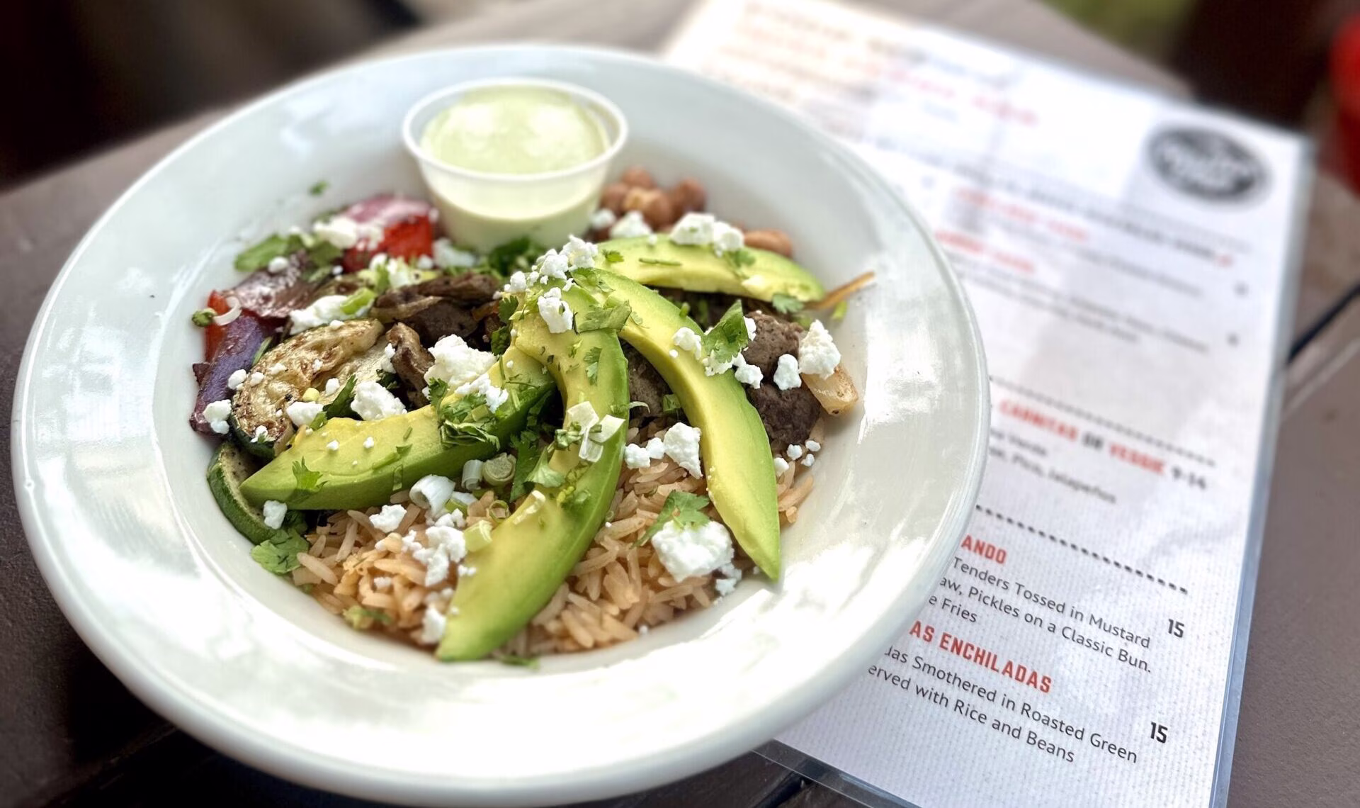 White bowl with rice, roasted vegetables, meat, avocado, and cheese.