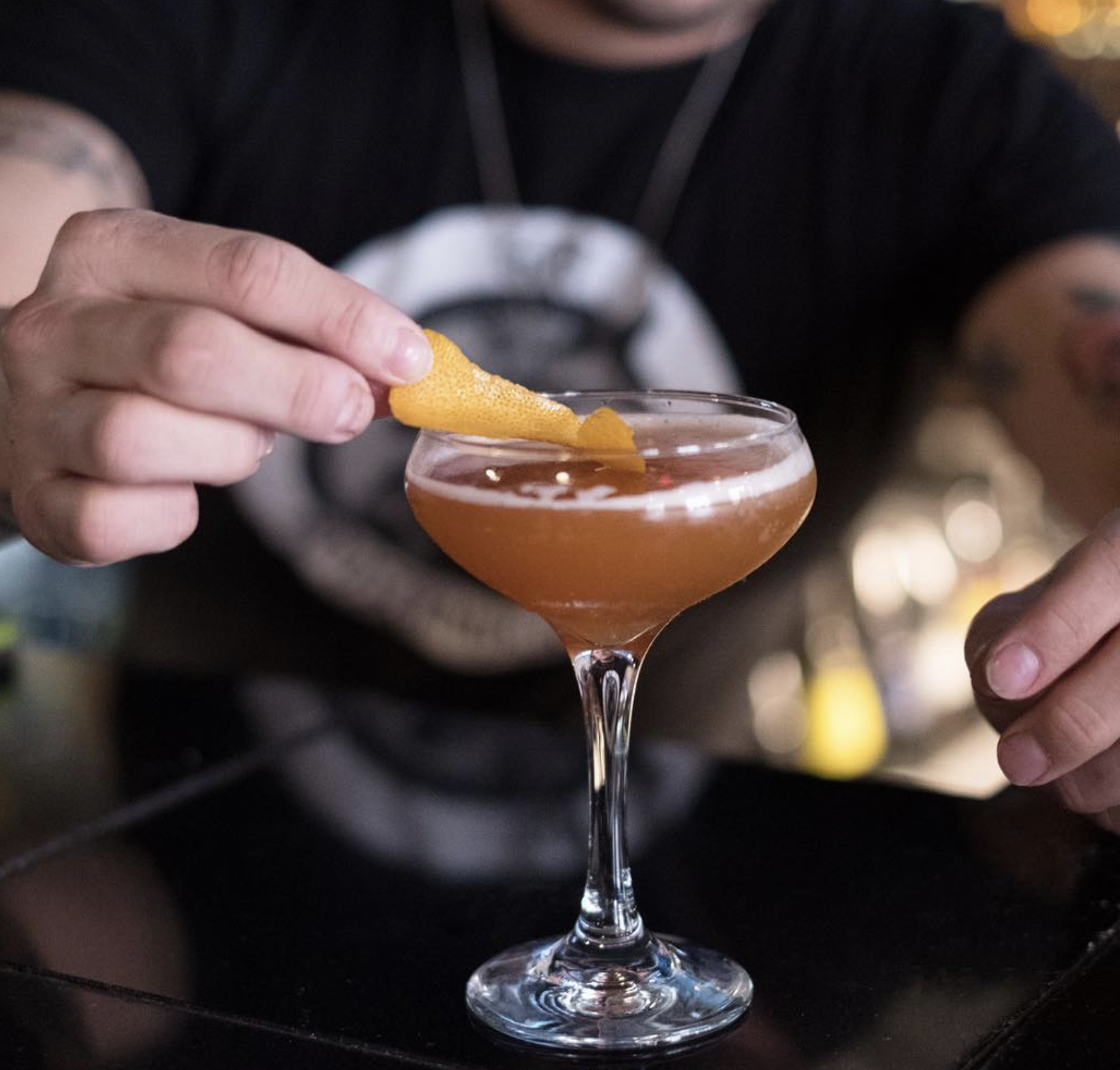 Hand places orange peel garnish on an amber cocktail glass.