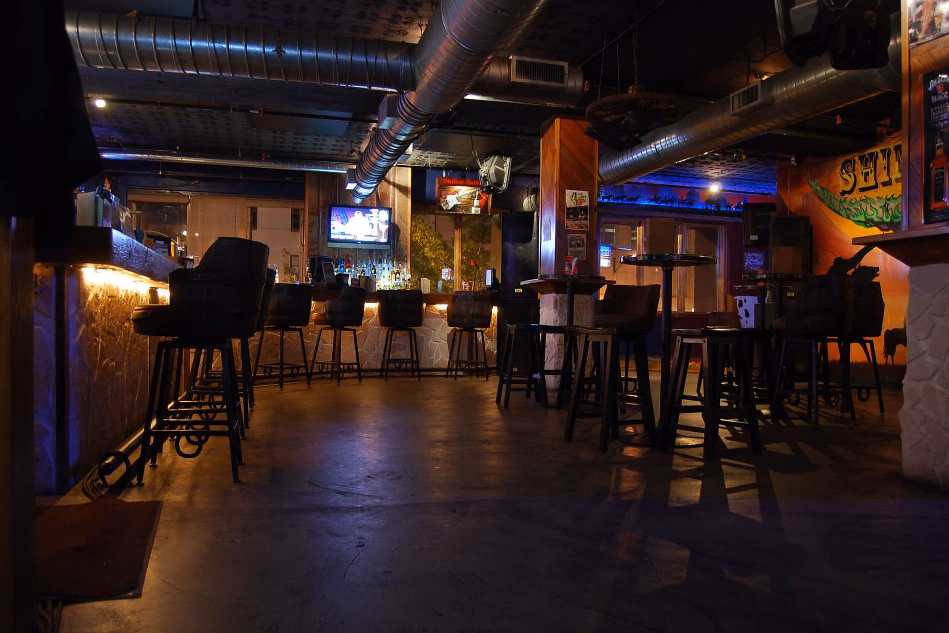 Empty, dimly lit bar with stools, tables, and Western decor.