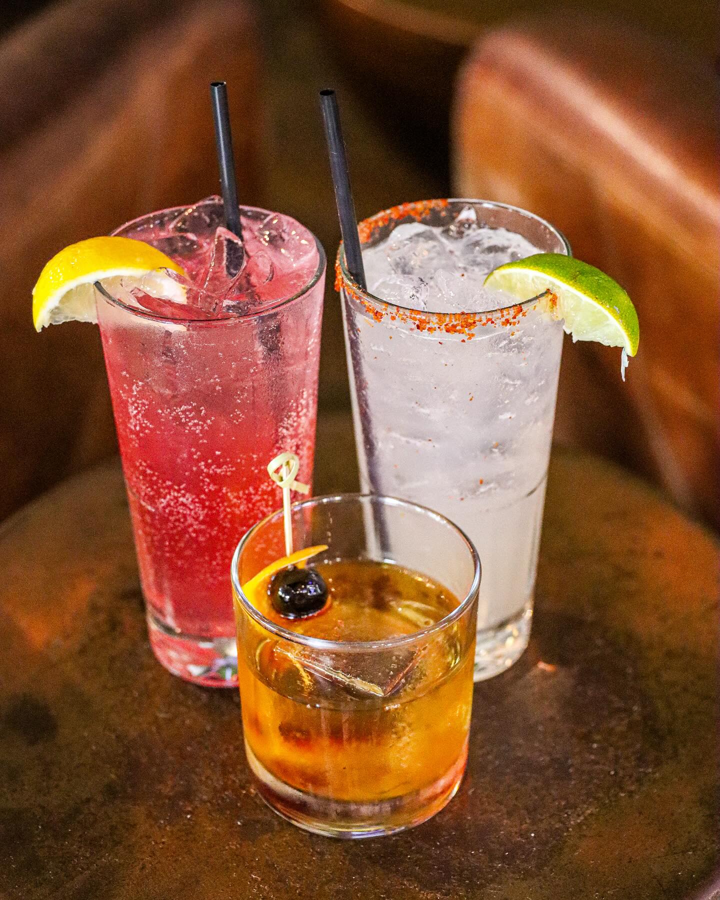 Three glasses of iced beverages with fruit garnishes on a table.