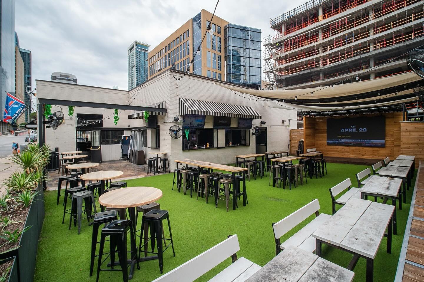 Outdoor bar patio with artificial turf, various tables, and city background.