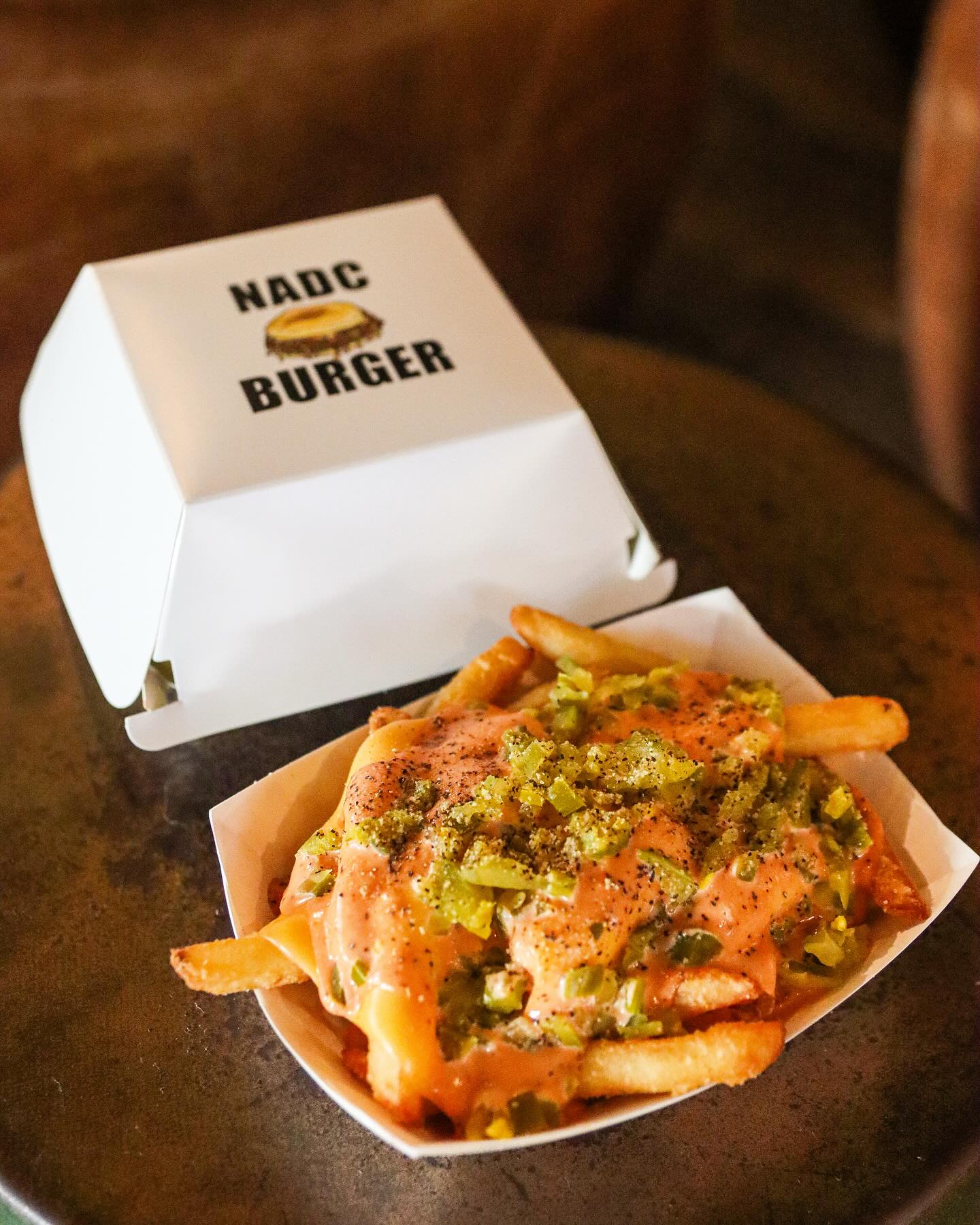 Loaded fries with sauce and green peppers next to NADC Burger box.