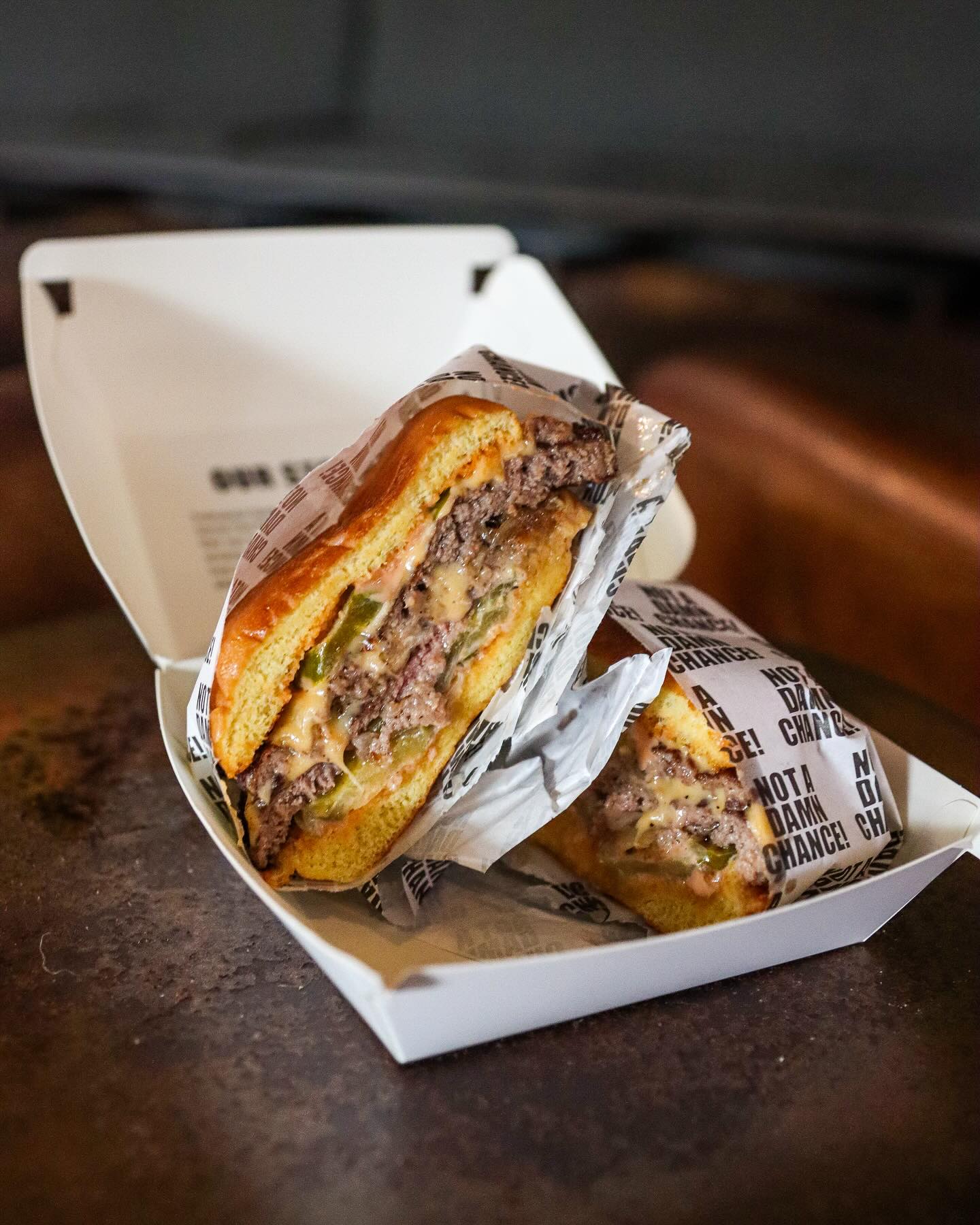 Two burgers in a white box, one cut in half showing fillings.