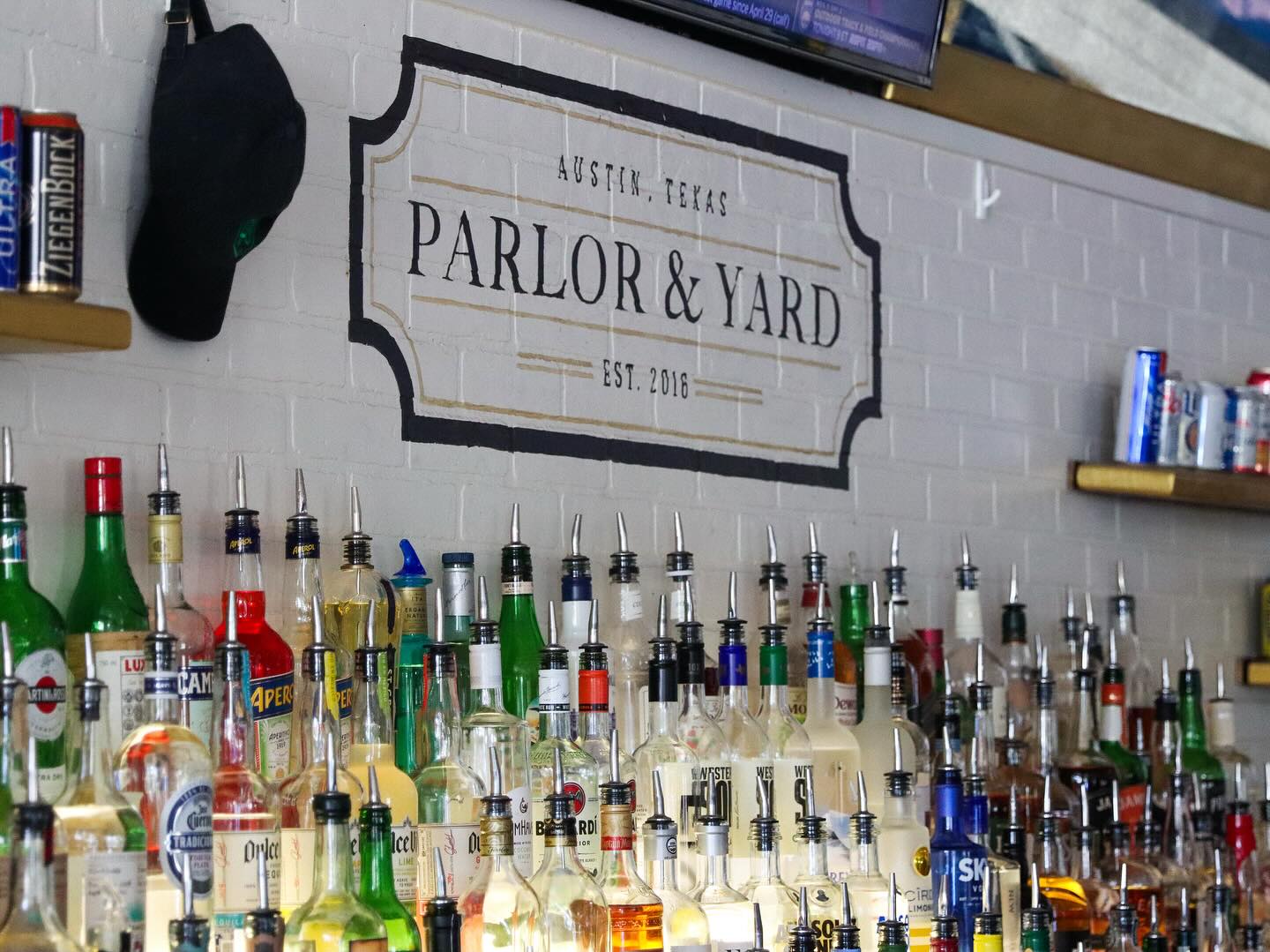 Many liquor bottles line a bar under the Parlor & Yard sign.