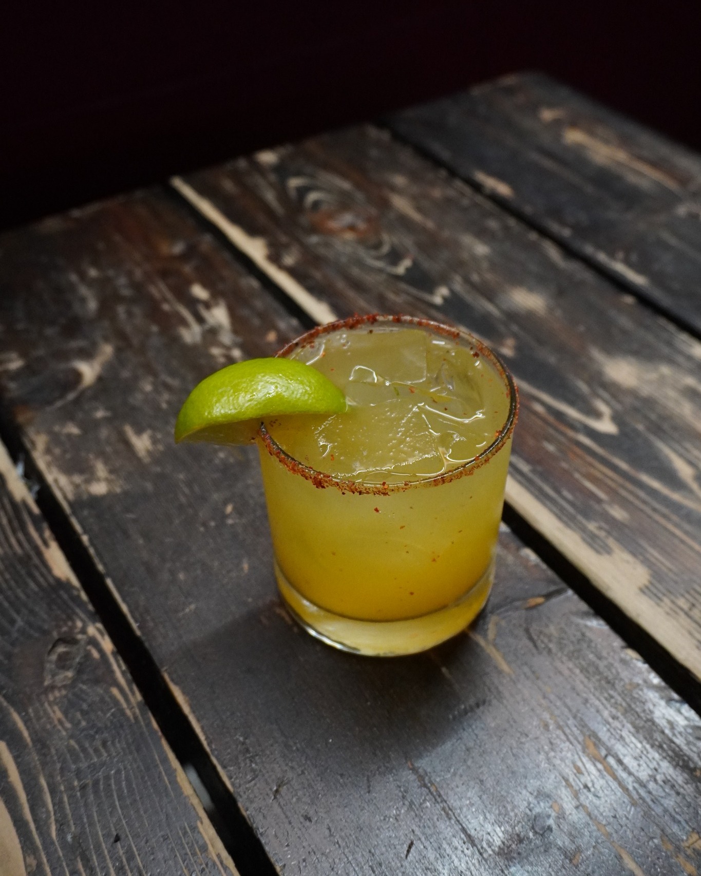 Yellow iced drink, chili-spiced rim, lime, on rustic wooden table.