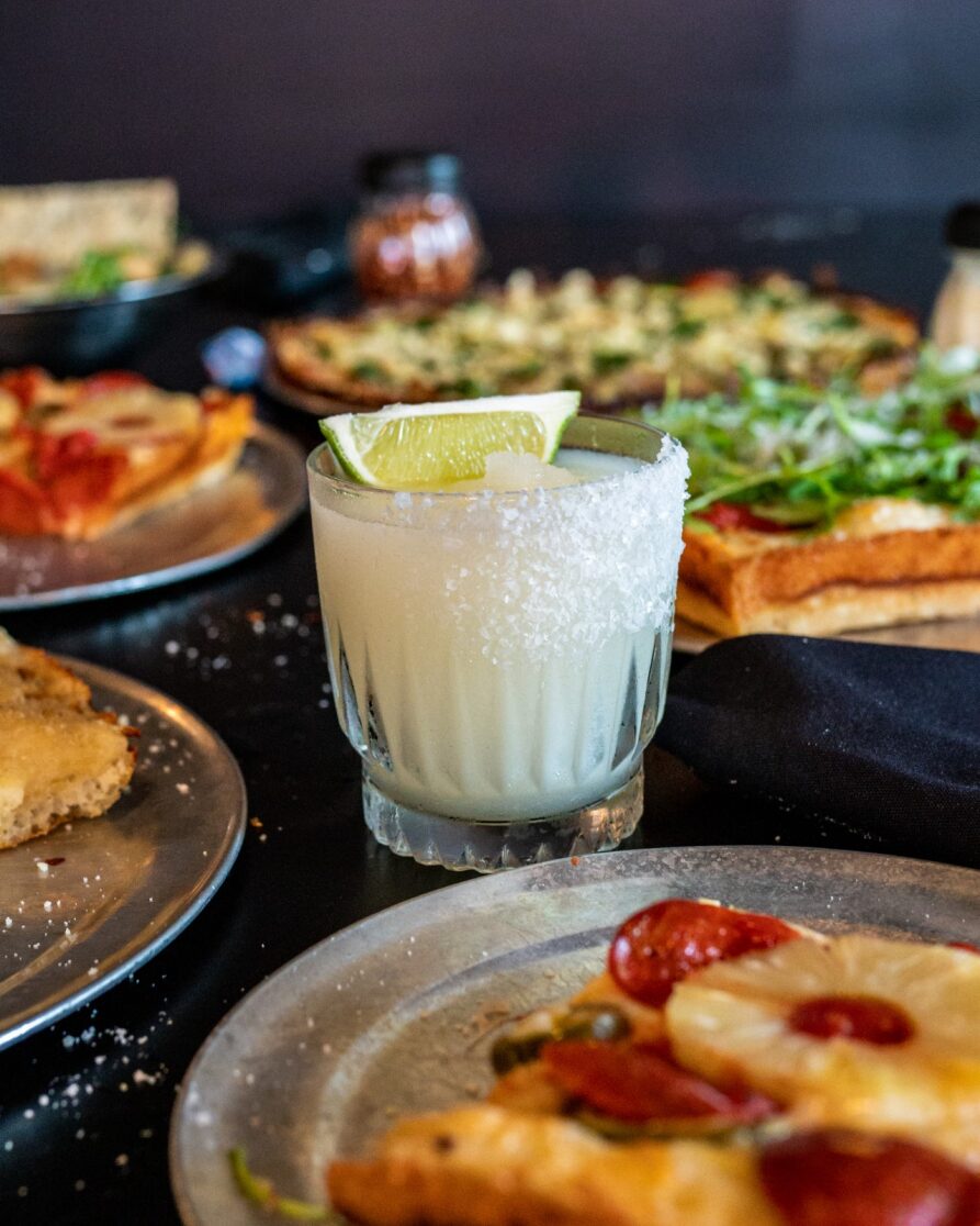 Frosty lime drink with salt rim, lime wedge, and food.