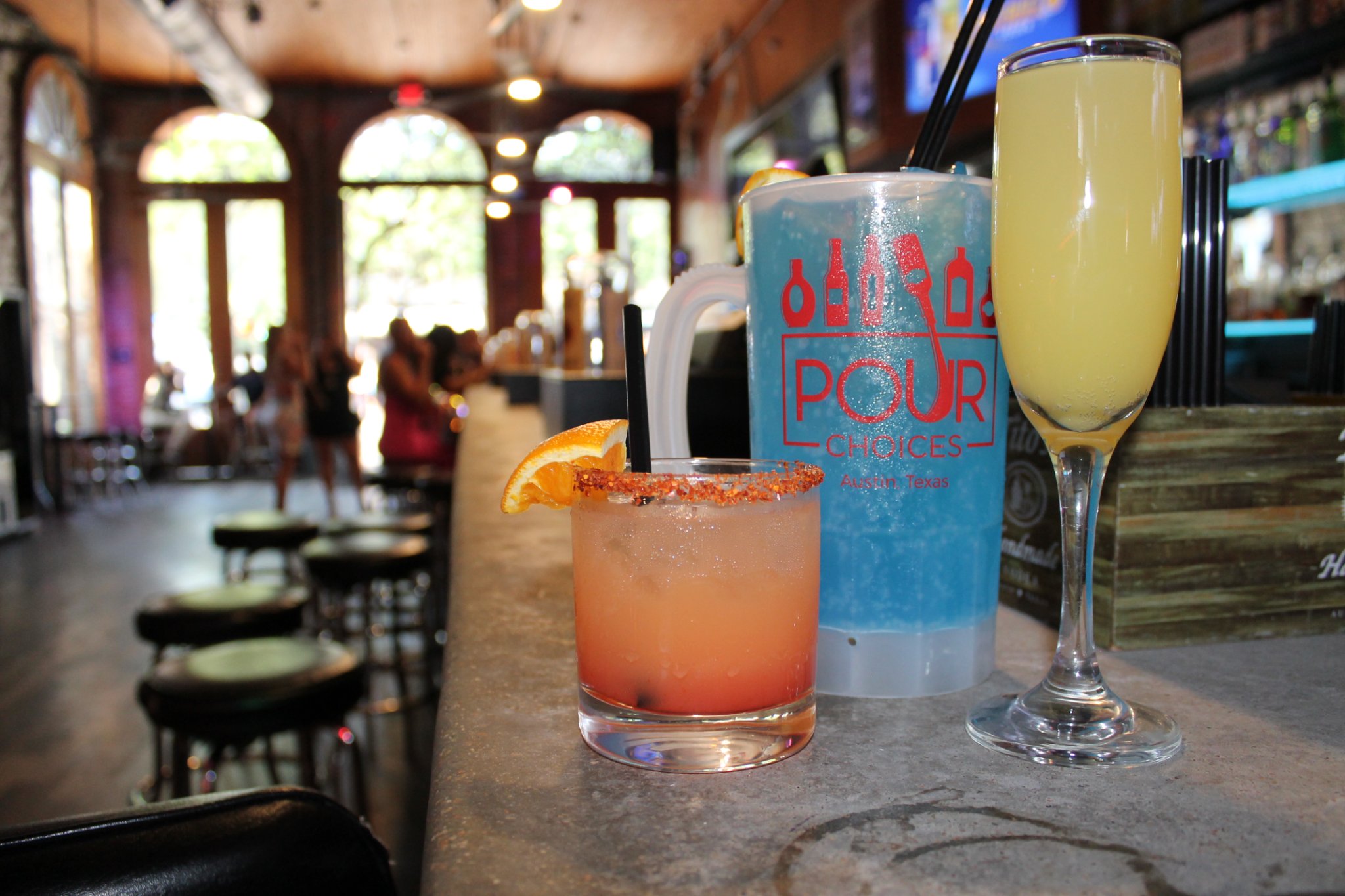Three drinks: a cocktail, a blue mug, and a mimosa on a bar counter.