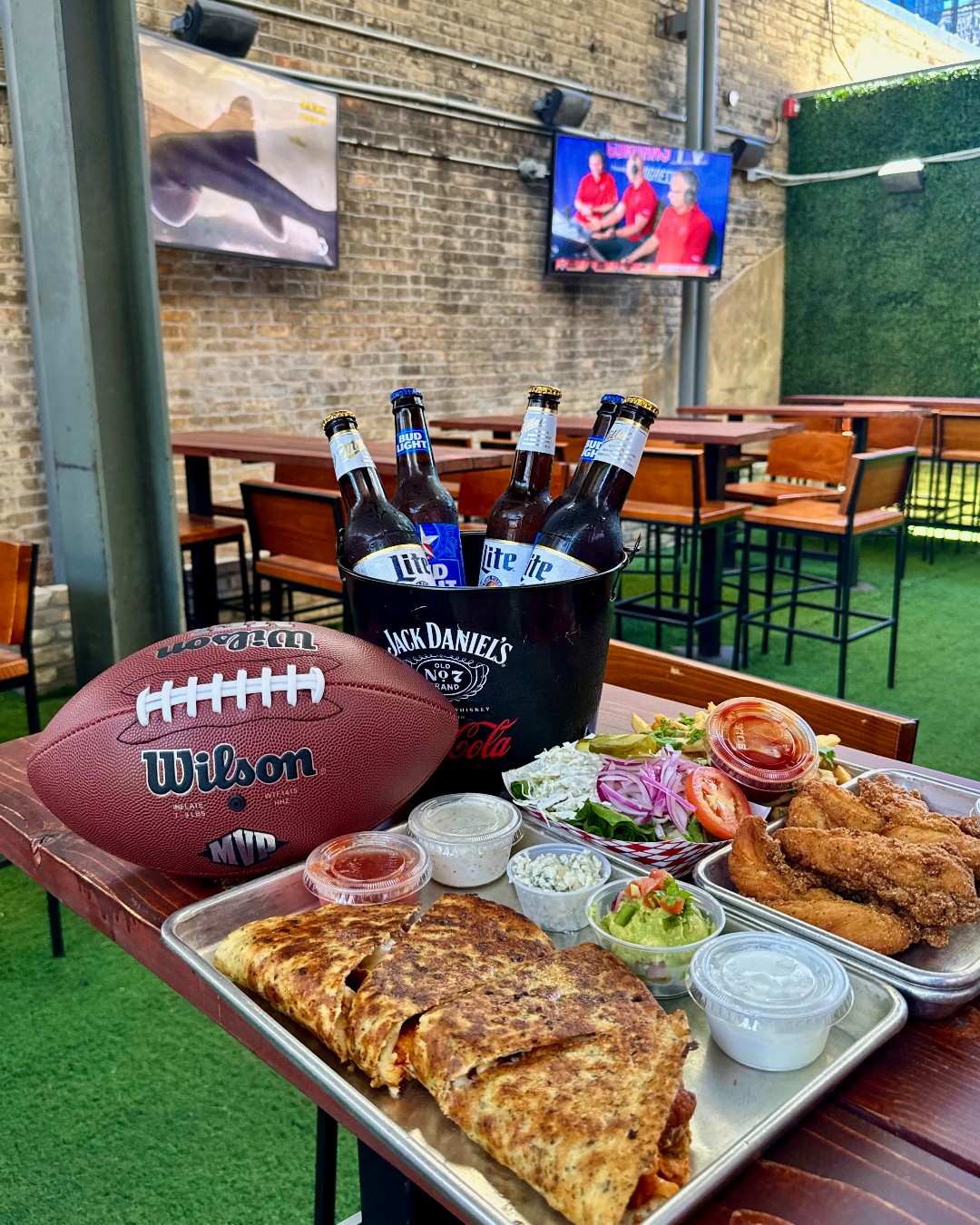 Outdoor sports bar table with football, bucket of beers, and food.