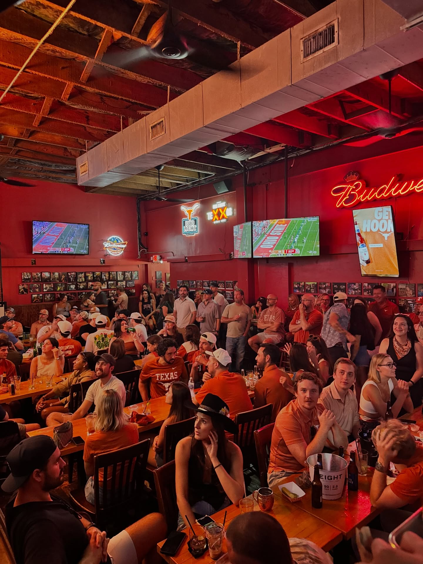 Fans wearing orange watching a football game in a crowded bar.