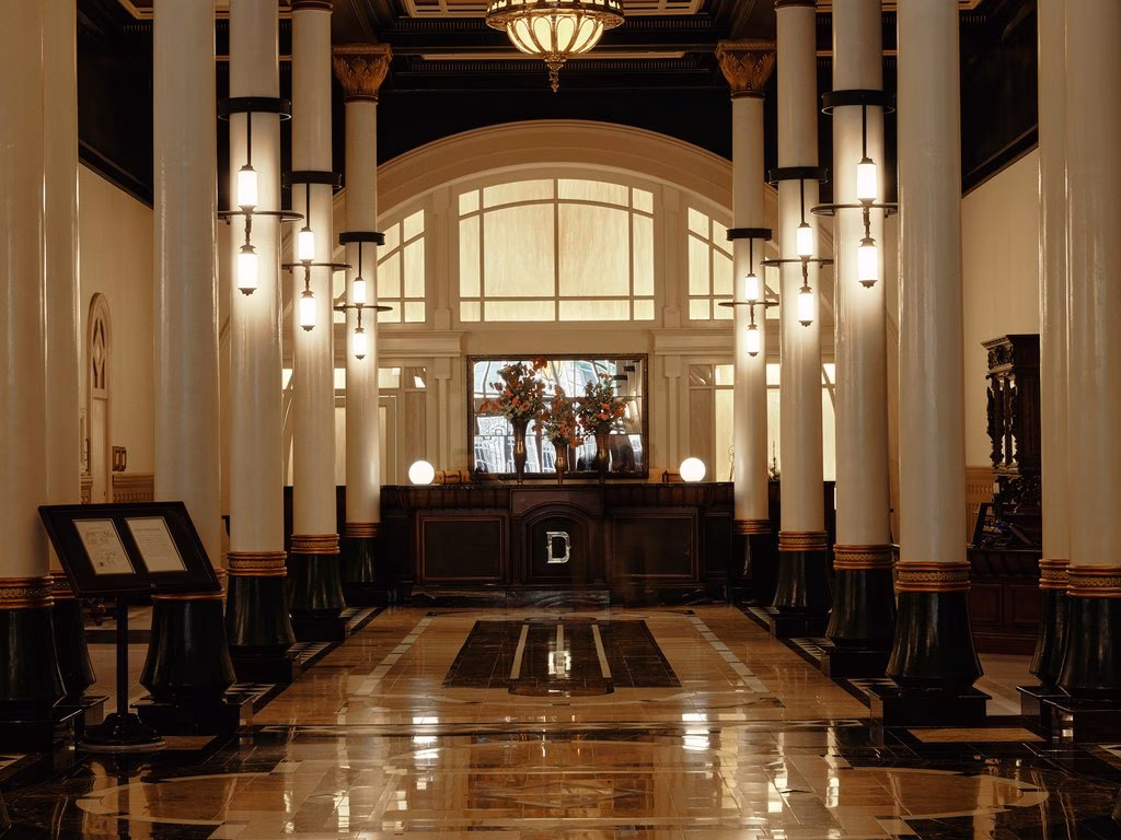 Columned hall with patterned floor, suspended lights, and large arched window.