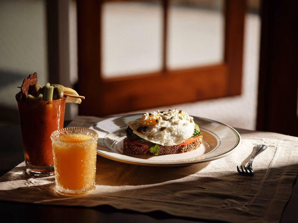 Egg toast, Bloody Mary, and orange juice on a sunlit table.