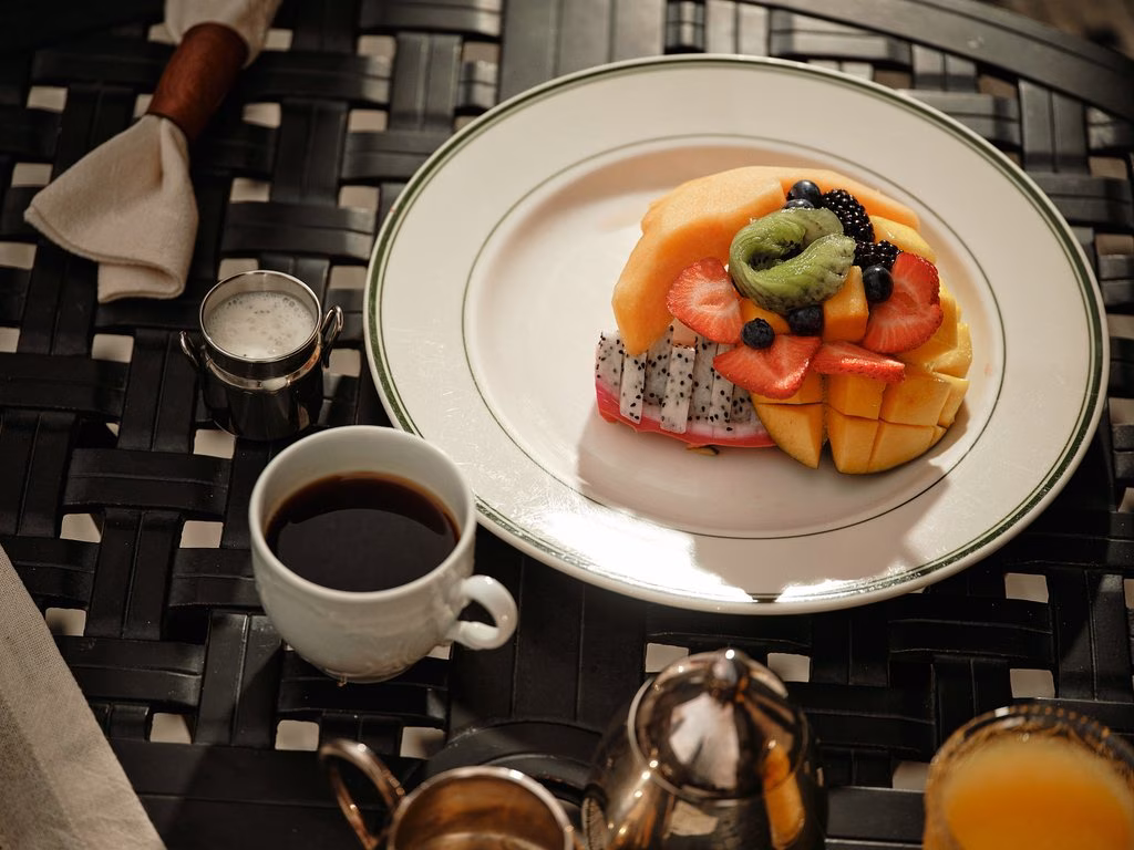 Fruit platter, coffee, milk, and orange juice on a dark table.