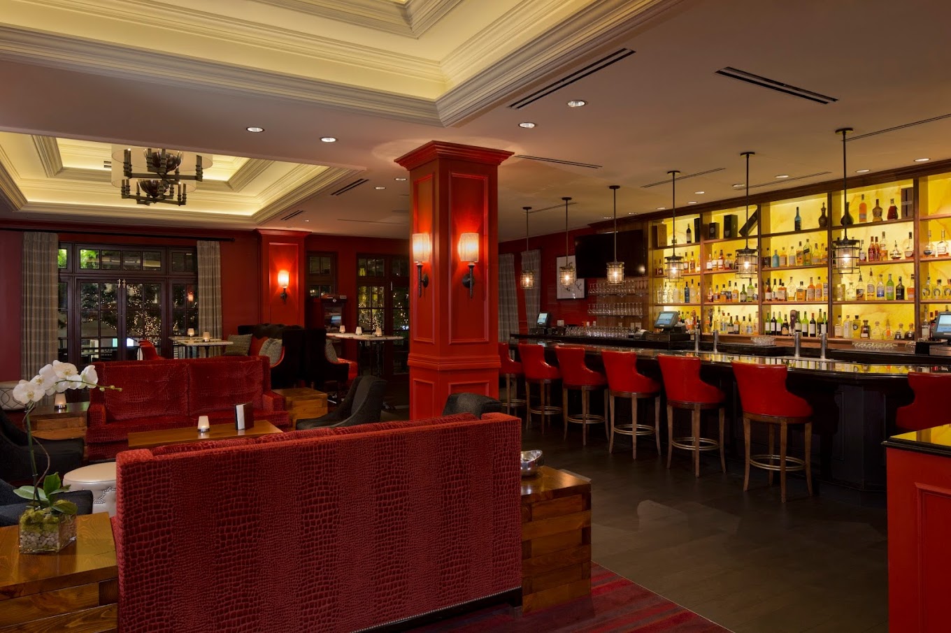 A bar and lounge area with red seating and illuminated liquor shelves.