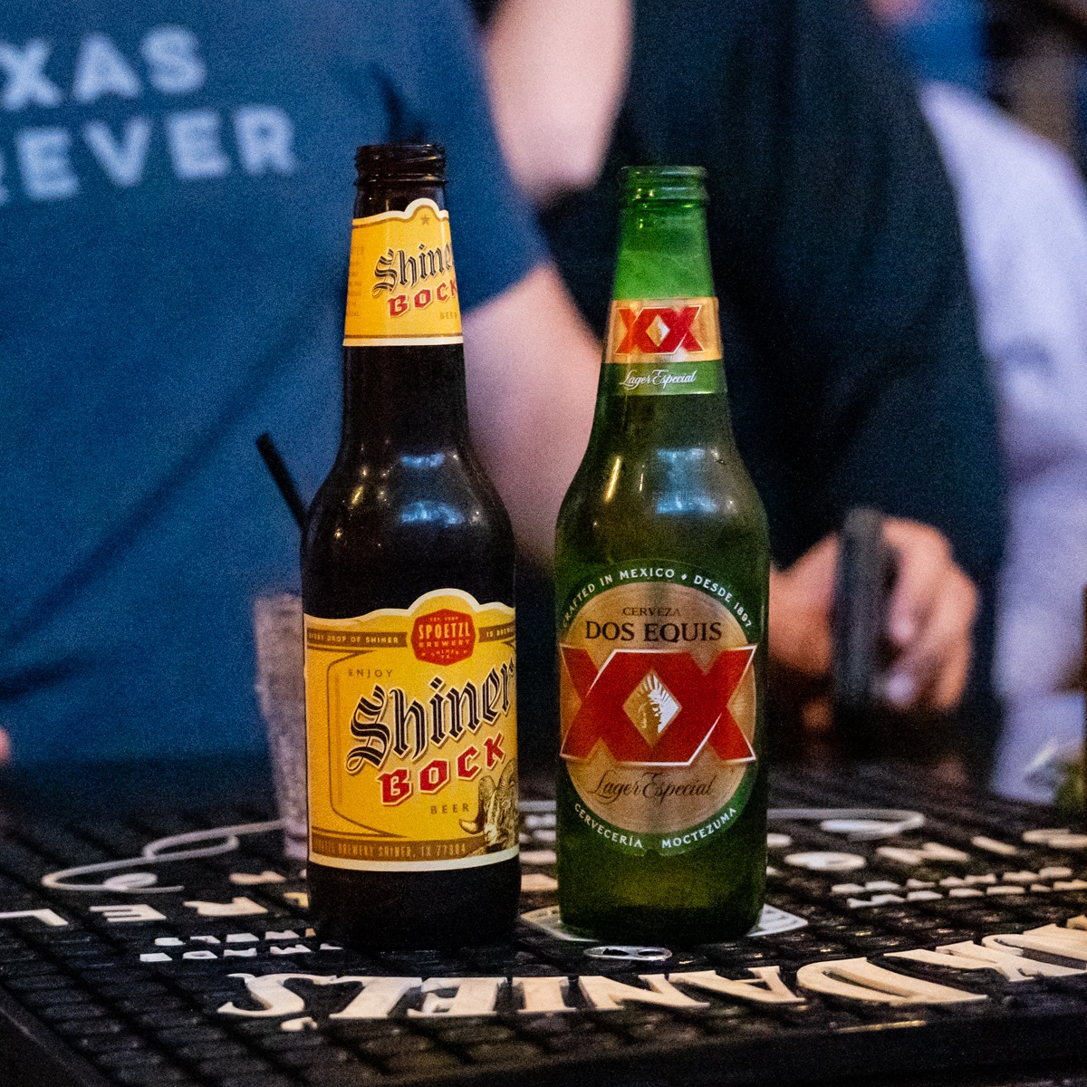 Two beer bottles, Shiner Bock and Dos Equis, on a bar mat.