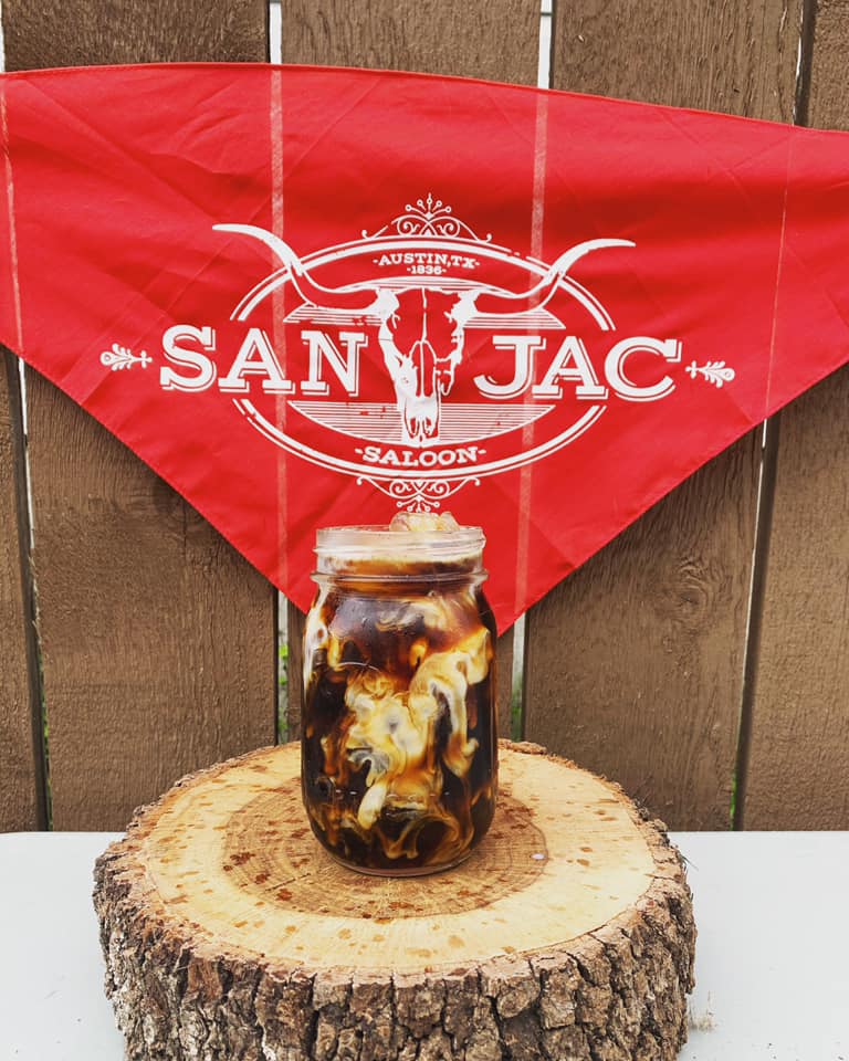 Mason jar with iced coffee and cream on log, red bandana.