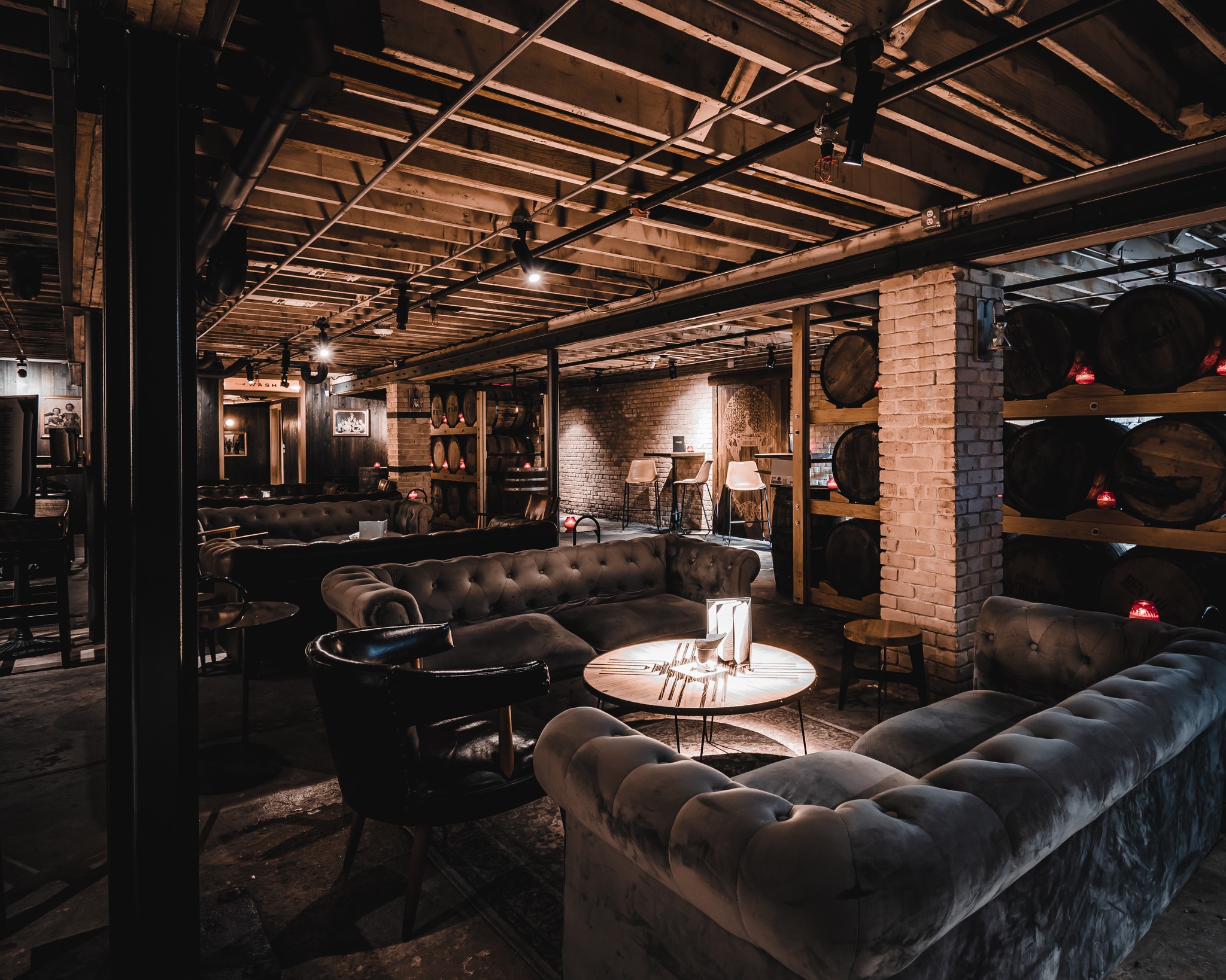 Cozy lounge with tufted sofas, exposed beams, and stacked barrels.
