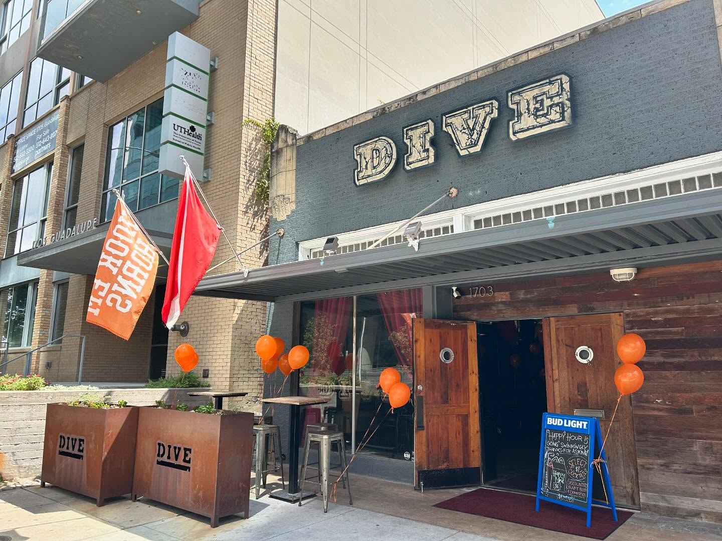 Dive bar entrance, wooden doors, orange balloons, and two flags.