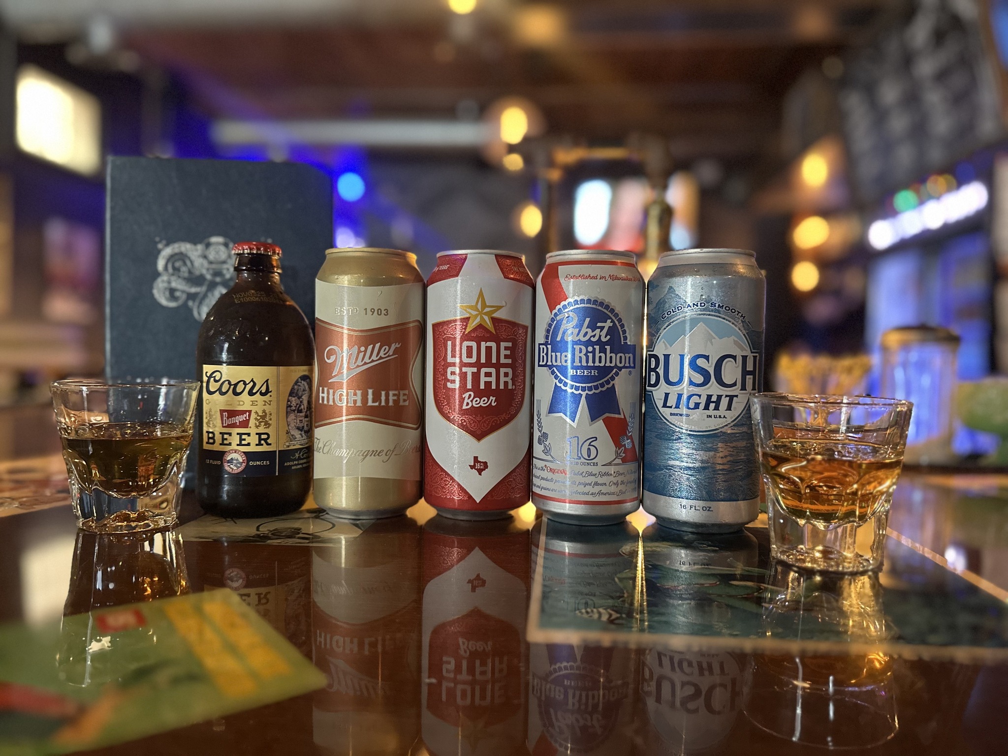 Five beers and two glasses of spirits on a reflective bar.