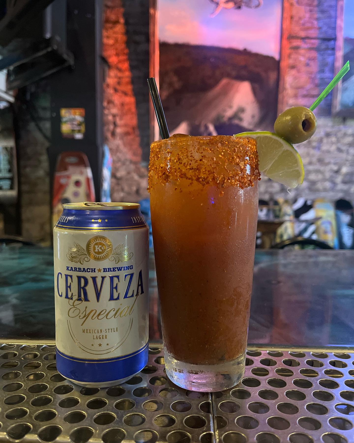 Spicy-rimmed drink with lime and olive, next to Karbach beer.