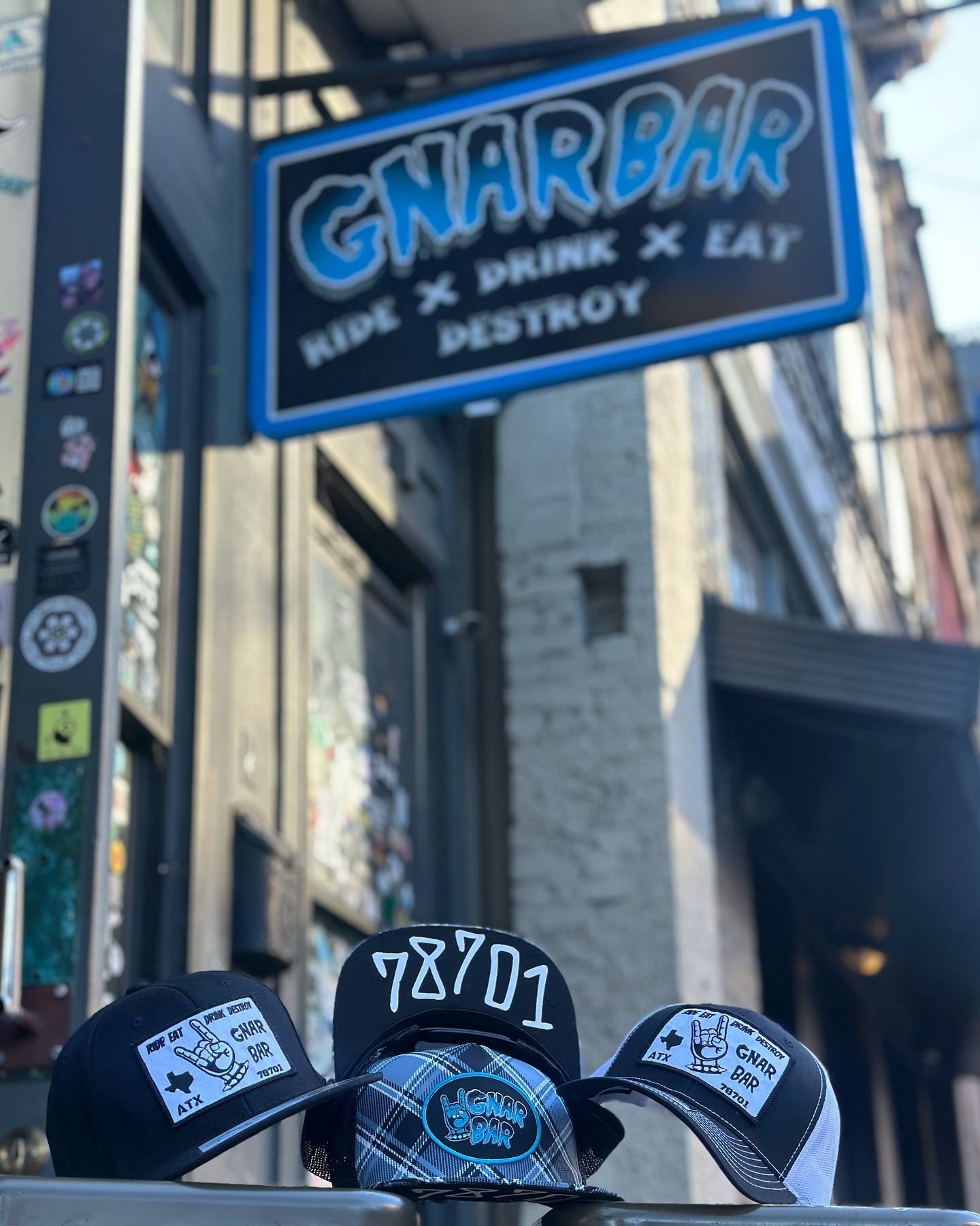 Three hats with GNAR BAR logos beneath a bar sign.