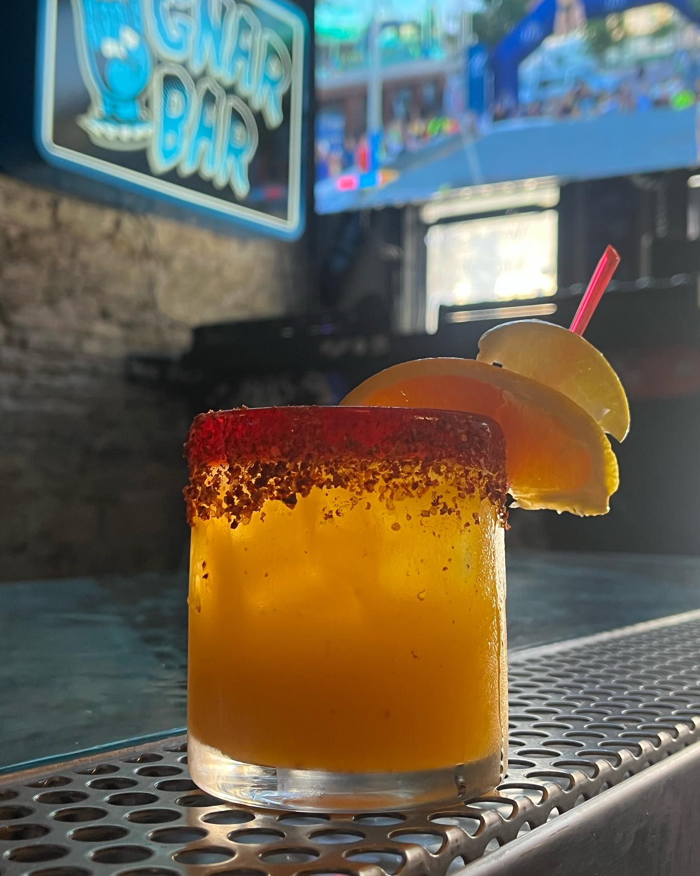 Orange drink with chili-rim and citrus slices on a bar counter.