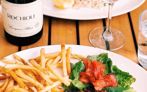 Bottle of Rochioli Sauvignon Blanc, french fries, and salad on a table.