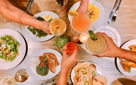 Overhead view: hands hold various drinks and food on a table.