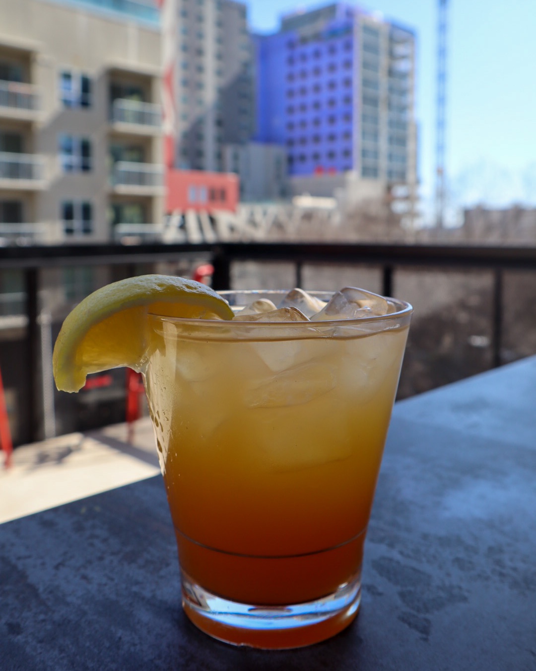 Iced gradient drink with lemon slice on table, city background.