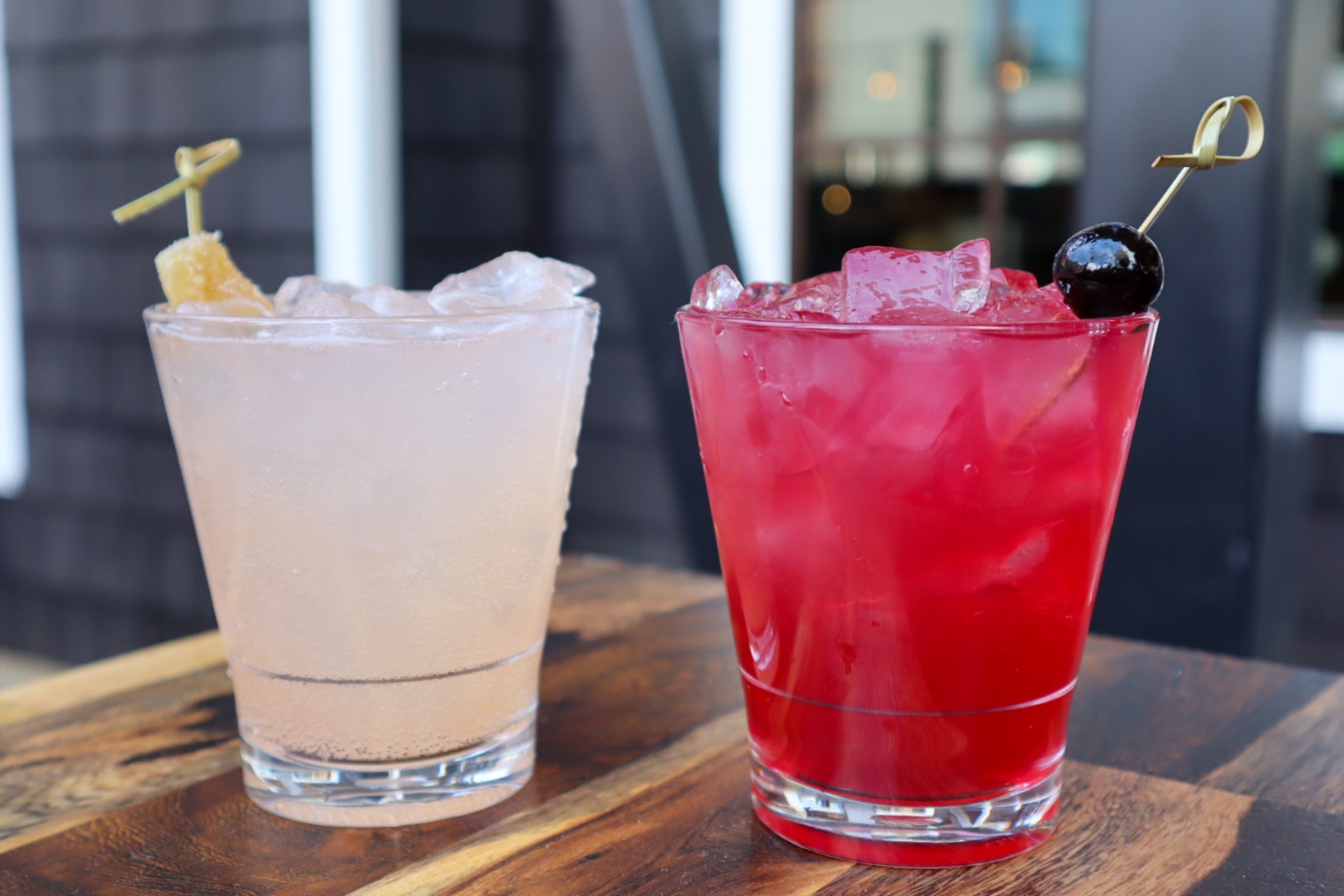 Two iced drinks, one light pink and one red, on a wooden table.