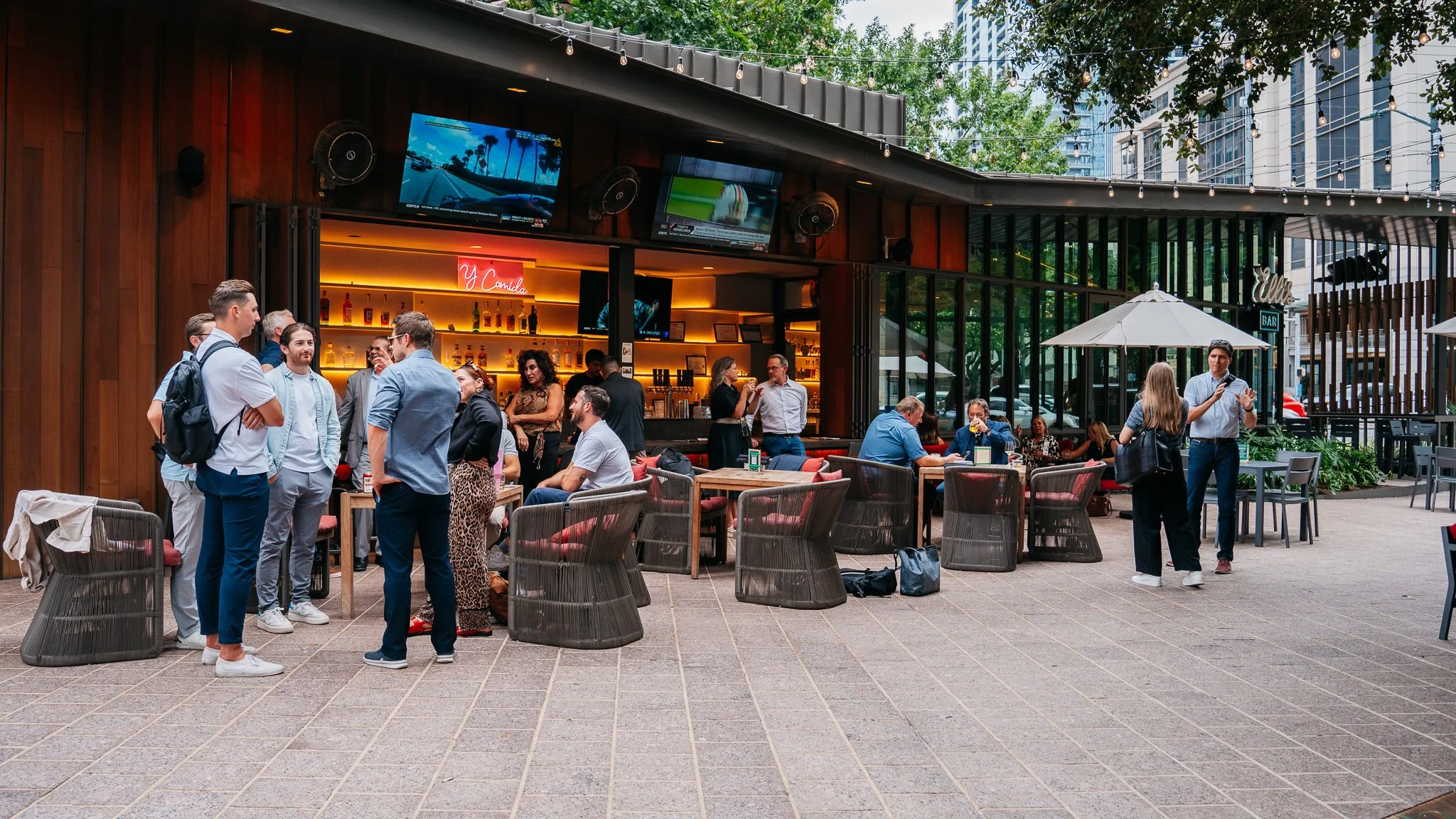 People socialize at an outdoor bar patio in a city setting.