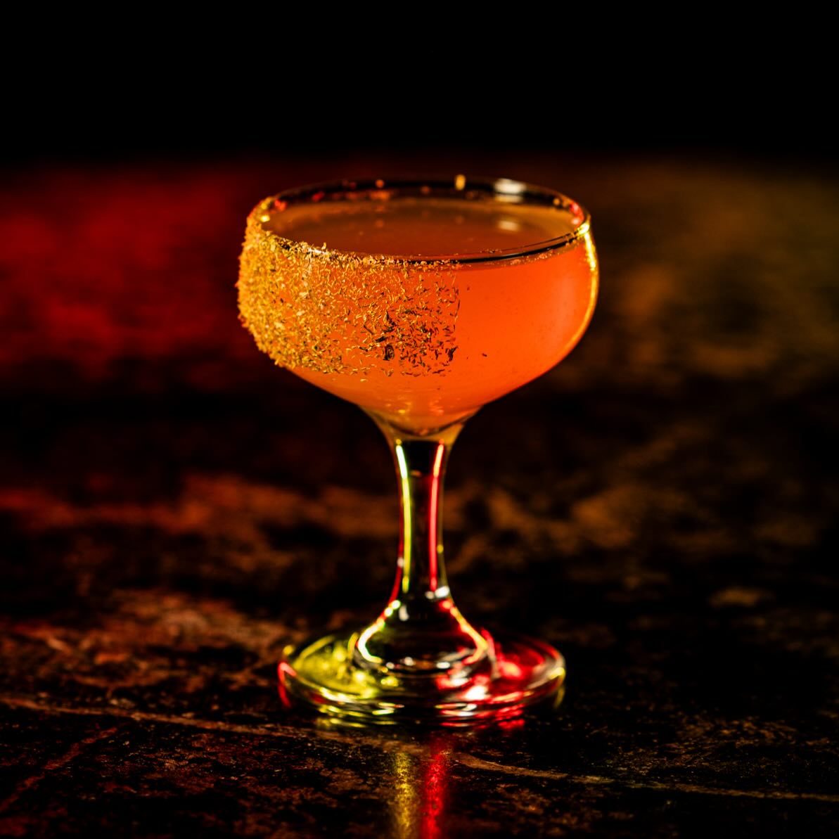 Orange cocktail in a sugared coupe glass, dark background.