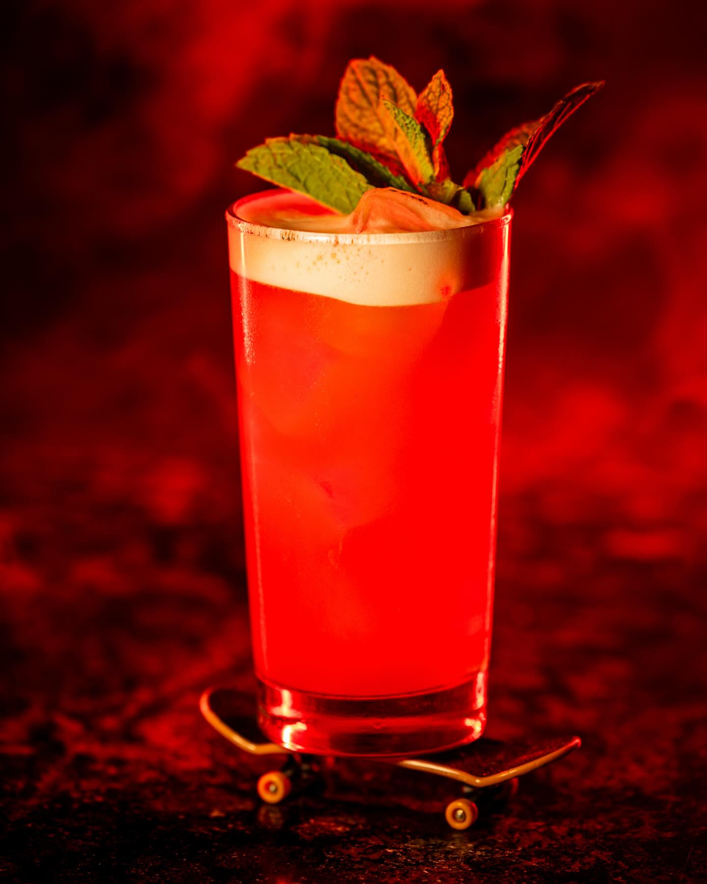 Red drink with mint leaves and foam on a miniature skateboard.