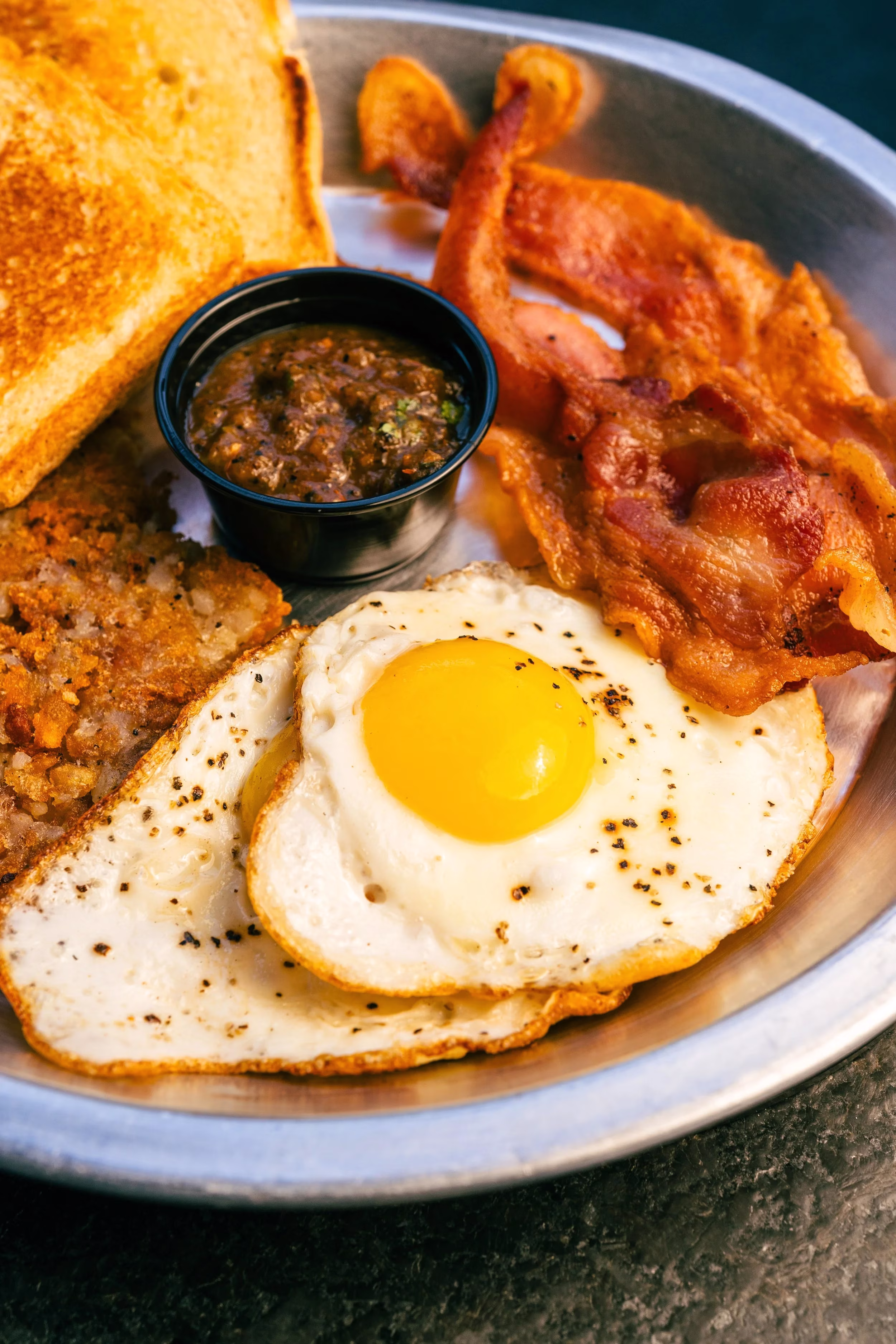 Breakfast plate with fried eggs, bacon, hash browns, toast, and salsa.