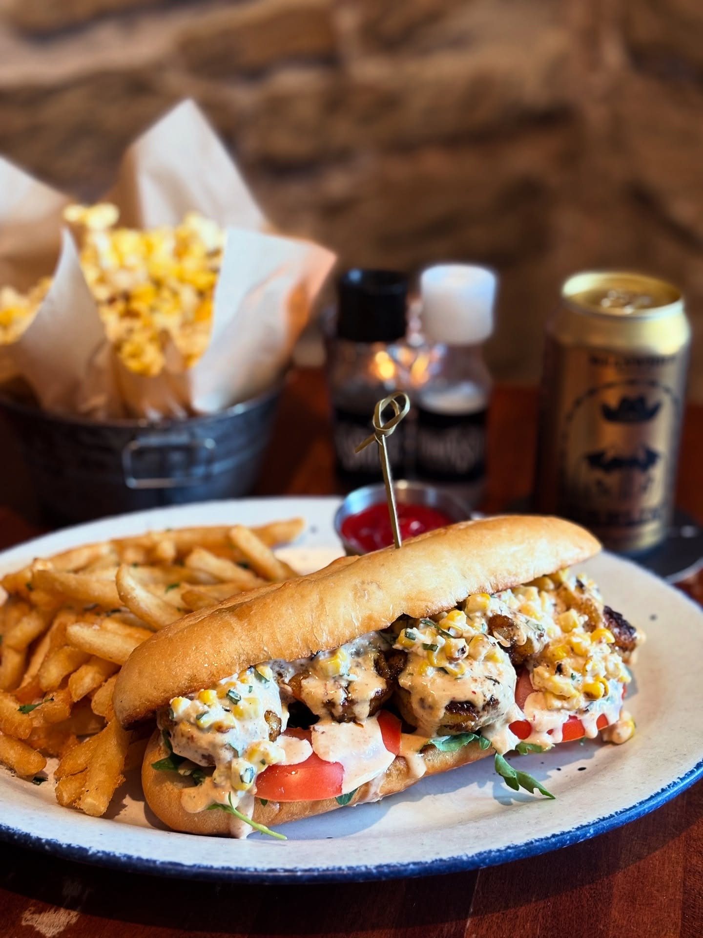 Sub sandwich with creamy corn topping, fries, ketchup, and popcorn bucket.