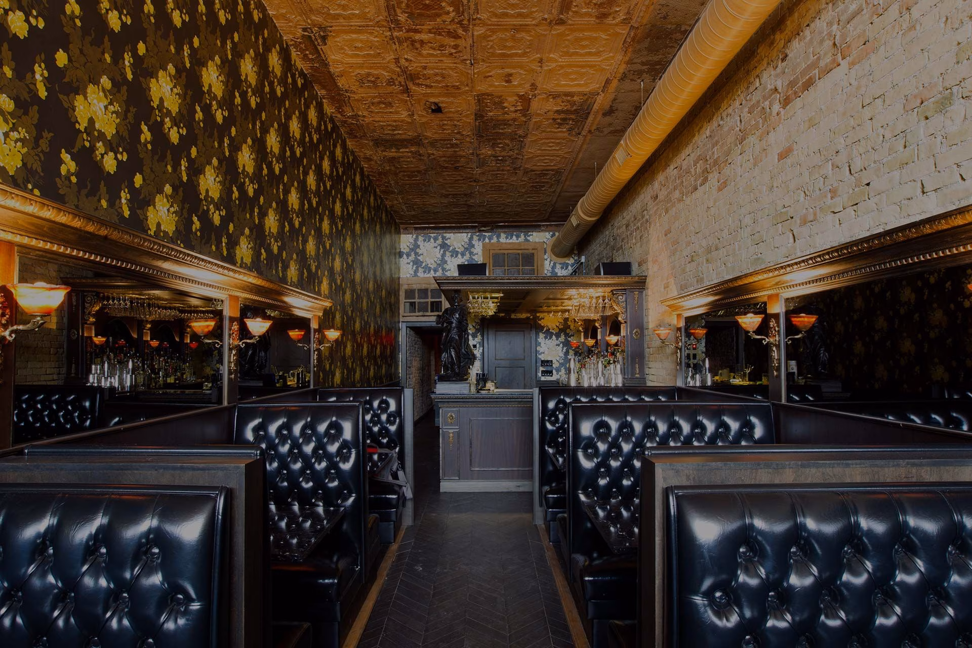Dimly lit restaurant with black leather booths, a tin ceiling, and brick wall.