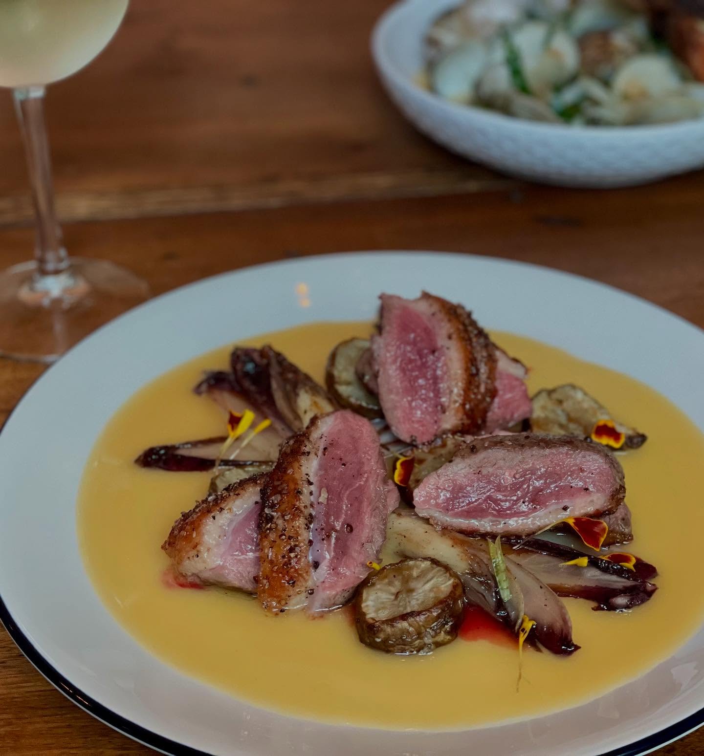 Sliced duck breast, pink inside, with yellow sauce and roasted vegetables.