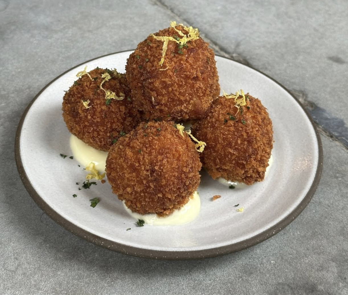Four breaded fried croquettes with white sauce, lemon zest, and herbs.
